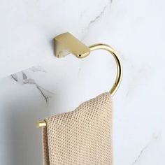 a gold towel holder on the wall next to a white marble counter top with a beige towel hanging from it