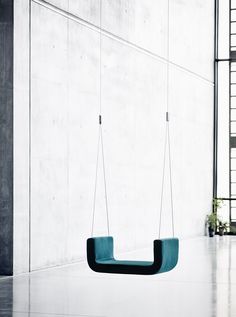 a green swing hanging from the ceiling in an empty room with concrete walls and windows