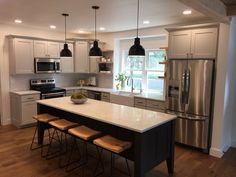 a kitchen with white cabinets and stainless steel appliances, including an island countertop that has four stools in front of it