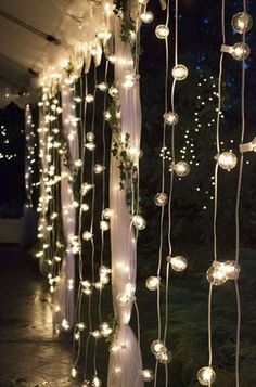 some lights hanging from the side of a building with white curtains and string lights on it