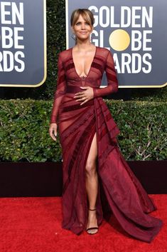 a woman in a red gown standing on a red carpet with her legs slited