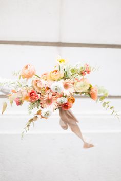 a bridal bouquet with orange and pink flowers hanging from it's side against a white wall