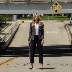 a woman standing in front of a street sign on the side of a road with her hands in her pockets