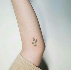 a woman's arm with a small leaf tattoo on the left side of her arm