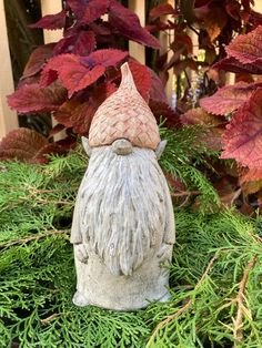 a gnome statue sitting on top of a lush green field next to red and purple leaves