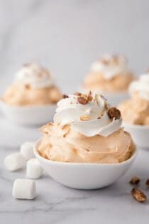 small bowls filled with whipped cream and marshmallows on a white tablecloth