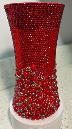 a red vase with lots of beads on the top and bottom is sitting on a white stand