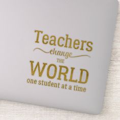 there is a white laptop with gold lettering on the screen and it says teachers change the world one student at a time