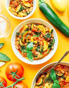 three bowls filled with different types of food on top of a yellow surface next to tomatoes, zucchini and other vegetables