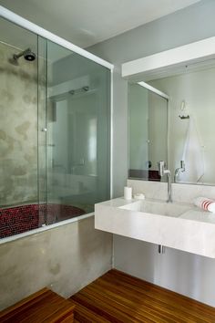 a bathroom with a sink, shower and wooden flooring in front of a large mirror