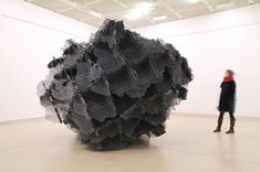 a person standing in front of a large black piece of art that looks like mesh