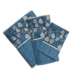 three blue napkins with embroidered leaves on them