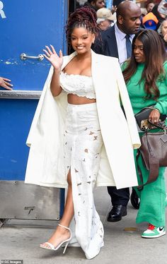 a woman in a white outfit waves to the crowd as she walks down the street