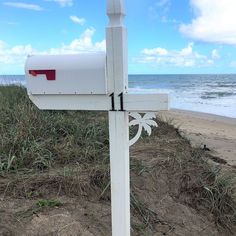 a white mailbox sitting on top of a sandy beach next to the ocean and grass