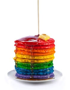 a stack of pancakes covered in rainbow icing with a wooden skewer sticking out of the top