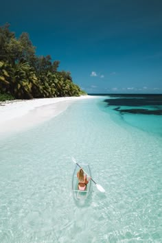 a woman in a boat on the beach with palm trees and clear blue ocean water