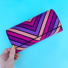 a woman's hand holding a pink, purple and black knitted clutch on a blue background