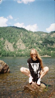 a woman sitting on top of a rock next to a body of water