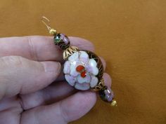 a hand holding a small white and red flower bead on a gold plated chain