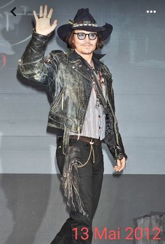 a man in a cowboy hat and leather jacket waves to the crowd at an event