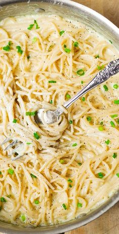 a bowl filled with pasta and peas on top of a wooden table next to a spoon