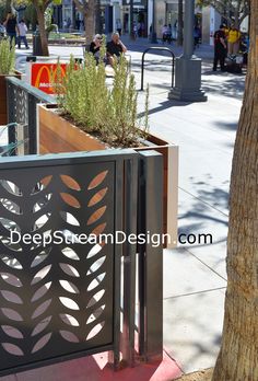 a metal gate on the side of a sidewalk next to trees and people walking by