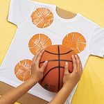 two hands holding a basketball over a mickey mouse t - shirt