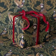 a gift box with a red ribbon tied around it sitting on a floral wallpaper