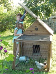 two children are standing in front of a chicken coop with their hands on the roof