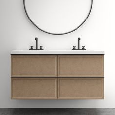 a bathroom vanity with two sinks and a round mirror on the wall above it, in front of a white wall