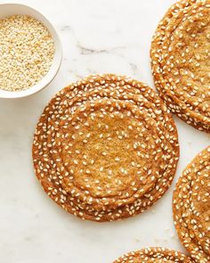 four sesame seed cookies next to a bowl of oatmeal on a marble surface