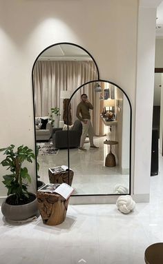 a man standing in front of a large mirror next to a potted plant on the floor