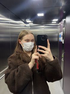 a woman wearing a face mask taking a selfie with her cell phone in an elevator