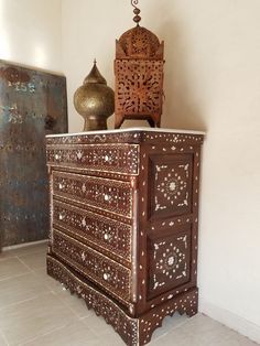 an ornate wooden dresser sitting on top of a tiled floor next to a vase and lamp