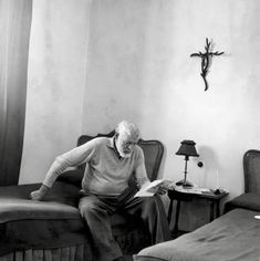 an old man sitting on a chair reading a book in a room with two beds