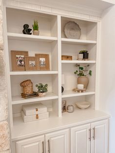 a white bookcase filled with lots of books next to a wall mounted vase and potted plant