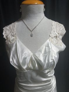 Vintage White satin shine wedding dress. Beautiful and radiant Ivory toned fabric paired with scroll and floral lace design starting at the shoulders and cascading over the open back and tapered into the back waist. Surplice cut bodice makes a shallow v cut neckline. Bust is shaped with darts and loose gathers to accentuate. Ruched waistline minimizes the waist. Sleeveless. The glowing fabric glides over the hips. Dress is floor length. Side zipper. Dress in good condition with a few minimal snags. Classic Jessica McClintock. Size 14. Fits like a 12.  *Accessories not included. Elegant Lace Trim Wedding Dress, Elegant Gown With Lace Trim And Sweetheart Neckline, Elegant Gown With Delicate Lace And Sweetheart Neckline, Elegant Gown With Sweetheart Neckline And Delicate Lace, Elegant Wedding Dress With Lace Trim And Fitted Bodice, Elegant Evening Wedding Dress With Ruched Bodice, Elegant White Gown For Mother Of The Bride, Elegant White Mother Of The Bride Gown, Elegant Evening Dress With Lace Back And Fitted Bodice