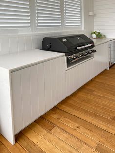 an outdoor kitchen with white cabinets and wood flooring on the outside wall, along with a built - in bbq