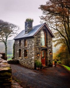 an old stone house with a chimney on the side and trees in the back ground