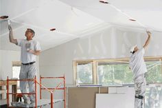 two men are painting the ceiling in an unfinished room