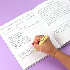 a woman's hand holding a yellow pen and writing on a book with purple background