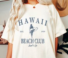 Vintage Hawaii Beach Club Tshirt, Comfort Colors Surfer Tee Shirt, Garment-Dyed Honolulu Oahu Apparel The Comfort Colors C1717 100% Ring Spun Cotton T-Shirt is very appropriately-named. All colors are inspired by nature and have a perfect lived-in, weathered look. Shirts are sent through a unique dyeing process that makes them incredibly soft and long-lasting. Each piece is soft-washed 50 times before making its way to you! Stitched at the collar, armhole, sleeves and bottom hem for ultimate durability, you will notice the density and quality of this shirt, but won't mind living in it. COMFORT COLORS 1717 ADULT TEE 6.1 Oz/SqYd 100% Ring Spun Cotton Soft-washed garment-dyed fabric Double-needle collar Twill taped neck and shoulders Twill label Relaxed fit Double needle armhole, sleeve and b Cute Beachy Shirts, Surf Tee Design, Beachy Graphic Tees, White Hawaiian Surfing Top, Beachy Tees, Beachy Tshirt, Beachy Shirts, Beach Tshirt Designs, Beach Shirt Design