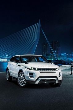 a white range rover parked in front of a city at night