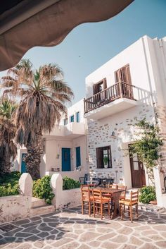 an outdoor dining area with table, chairs and palm trees in front of a white building