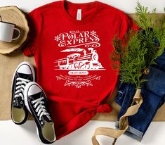 "Polar Express Christmas Shirt, Polar Express Ticket Shirt, Train Depot Shirt, North Pole Shirt, Christmas Holiday Shirt, Polar Express Shirt  Product * Non-Heather shirts are 4.2 oz. and 100% cotton * Heather Shirts are 4.2 oz. and 52/48 cotton/polyester * Unisex sizing * Coverstitched collar and sleeves * Heat transfer label * Machine wash warm, with like colors * Medium iron Important * Please review shirt size and color options before ordering. * If you want to order different colors (which one is not available in the options), long-sleeve shirts, sweatshirts, etc..., please contact us, and we help you. * Our most important goal is to make sure you are a happy customer that received everything you were expecting. Please give us a chance to resolve any problem by contacting us before le Christmas Graphic Tee Shirt In Cotton, Christmas Cotton Graphic Tee Shirt, Red Short Sleeve Shirt For Winter, Polar Express Shirt Ideas, Polar Express Ticket, Polar Express Tickets, Polar Express Christmas, Cricut Corner, Polar Express Train