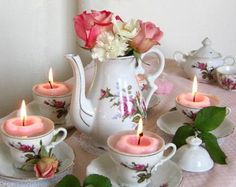 a table topped with tea cups and saucers filled with pink candles next to flowers