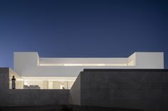 the exterior of a modern house with concrete walls and windows at night, as well as a person standing outside