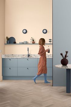 a woman in a pink dress is walking into a kitchen with blue cabinets and counter tops