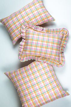 three plaid pillows with ruffled edges on a white surface, one is orange and the other is pink