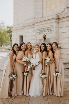 a group of women standing next to each other in front of a building holding bouquets